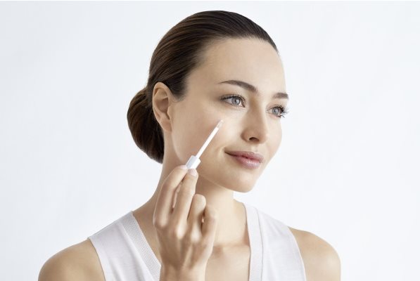 Frau trägt mit Pipette etwas auf ihr Gesicht auf