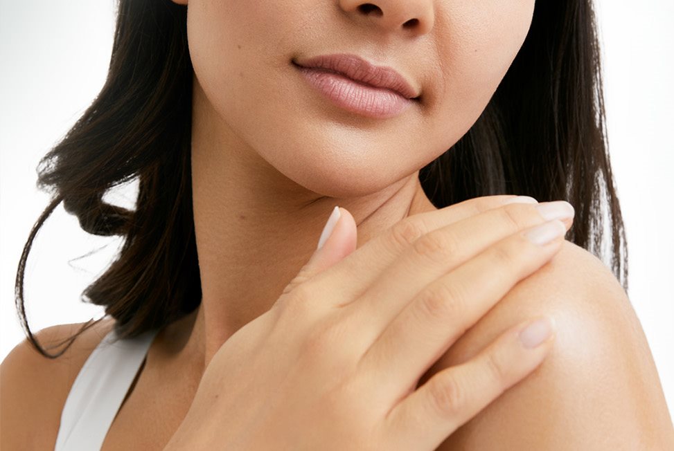 View of a female model with short dark hair touching her left shoulder and looking downwards against a white background.