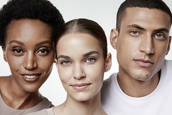 A closeup view of two female models and one male model wearing light coloured tops against a white background.