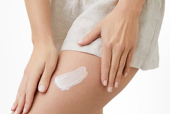 Gros plan d'une femme mannequin portant un short de couleur pâle et montrant du produit en crème étendu sur sa cuisse gauche.
